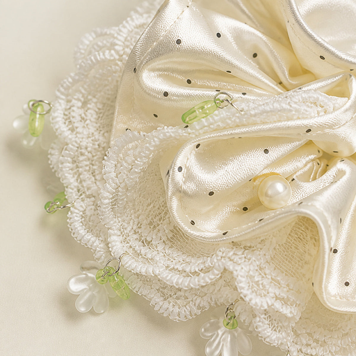 Close-up of ivory polka-dot satin, white lace trim and floral charm details