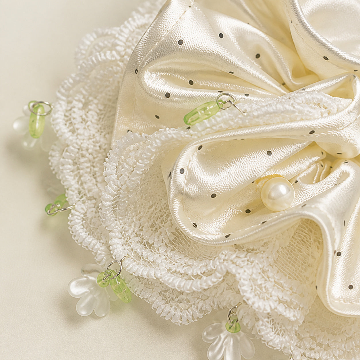 Close-up of ivory polka-dot satin, white lace trim and floral charm details